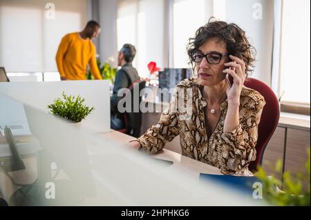 Ältere Frau, die in einem Büro telefoniert. Stockfoto