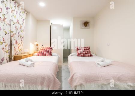 Schlafzimmer mit zwei Betten mit rosa Decken, roten Kissen, Rollhandtüchern und auffälligen Netzvorhängen in einer Ferienwohnung Stockfoto