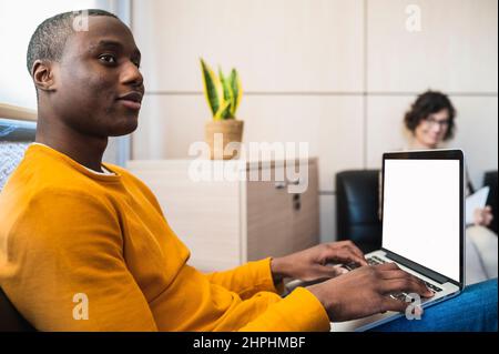 Schwarzer junger Mann, der in einem Büro auf einem Laptop tippt. Stockfoto