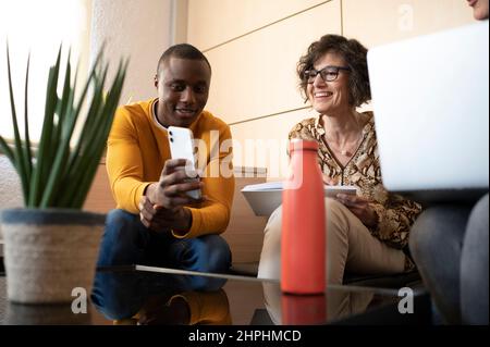 Schwarzer Mann zeigt seinem Kollegen etwas Lustiges auf seinem Handy. Stockfoto