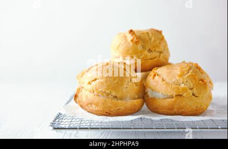 Selbstgemachte Profiterolen auf einem Metallgitter auf weißem Holzhintergrund. Stockfoto