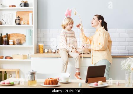 Portrait einer jungen Frau, die zu Ostern ein Haus mit niedlichem kleinen Jungen dekoriert, der Hasenohren trägt, Platz zum Kopieren Stockfoto