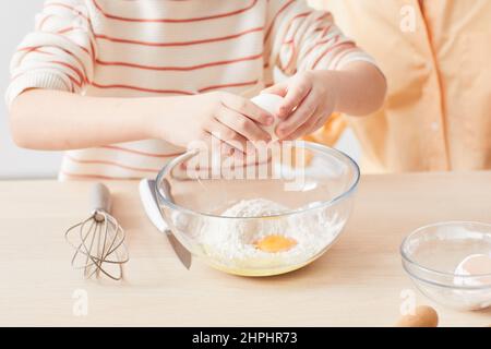 Nahaufnahme von Kindern, die Eier brechen, während sie Mutter beim Backen in der Küche helfen, Platz kopieren Stockfoto