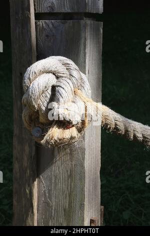 Ausgefranste Seil in einem Knoten auf einem verwitterten Holzpfosten gebunden. Stockfoto