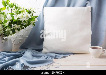 Quadratisches Baumwollkissen-Mockup mit Apfelblütenzweigen, blauem Schal und einer Tasse Kaffee. Kissenbezug aus rustikalem Leinen zur Designpräsentation Stockfoto