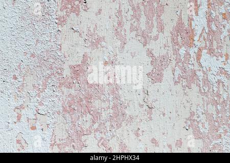 Gesprungene, verputzte Betonwand mit Überresten von weißer und rosa Farbe, strukturierter Hintergrund für Ihr Design. Stockfoto