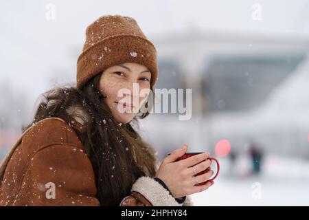 Junge süße asiatische Frau sitzt auf Bahnsteig mit Tasse heißen Tee in verschneiten Winterwetter Stockfoto