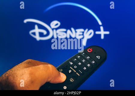 Brasilien. 21st. Februar 2022. In dieser Abbildung sehen Sie eine Nahaufnahme einer Hand, die eine TV-Fernbedienung hält, die vor dem Disney (Plus)-Logo angezeigt wird. Kredit: SOPA Images Limited/Alamy Live Nachrichten Stockfoto