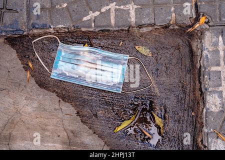 Eine chirurgische Maske, die als Schutz gegen COVID verwendet wird und in einer kleinen Wasserpfütze auf der Straße weggeworfen wird. Konzept der Pandemie, Pflege, Ende der Pandemie. Stockfoto