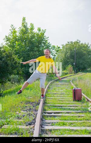 Langhaarige Brünette Reisende mit einem Koffer auf den Schienen geht Stockfoto