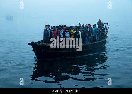 Narayanganj, Dhaka, Bangladesch. 22nd. Februar 2022. Arbeiter überqueren den Fluss Shitalakhya auf Holzbooten, um an einem nebligen Wintermorgen in Narayanganj, Bangladesch, ihren Arbeitsplatz zu erreichen. Dieser Fluss wird täglich von Millionen von Arbeitern als Route in das dicht besiedelte Stadtgebiet genutzt. Die Holzschiffe werden verwendet, um Menschen über den Fluss Shitalakhya zu transportieren, der am Rande der Stadt Narayanganj fließt. (Bild: © Joy Saha/ZUMA Press Wire) Stockfoto