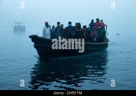 Narayanganj, Dhaka, Bangladesch. 22nd. Februar 2022. Arbeiter überqueren den Fluss Shitalakhya auf Holzbooten, um an einem nebligen Wintermorgen in Narayanganj, Bangladesch, ihren Arbeitsplatz zu erreichen. Dieser Fluss wird täglich von Millionen von Arbeitern als Route in das dicht besiedelte Stadtgebiet genutzt. Die Holzschiffe werden verwendet, um Menschen über den Fluss Shitalakhya zu transportieren, der am Rande der Stadt Narayanganj fließt. (Bild: © Joy Saha/ZUMA Press Wire) Stockfoto