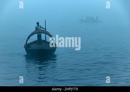 Narayanganj, Dhaka, Bangladesch. 22nd. Februar 2022. Ein Bootsmann rudert sein Boot auf dem Shitalakhya River während eines nebligen Wintermorgens in Narayanganj, Bangladesch. Dieser Fluss wird täglich von Millionen von Arbeitern als Route in das dicht besiedelte Stadtgebiet genutzt. Die Holzschiffe werden verwendet, um Menschen über den Fluss Shitalakhya zu transportieren, der am Rande der Stadt Narayanganj fließt. (Bild: © Joy Saha/ZUMA Press Wire) Stockfoto