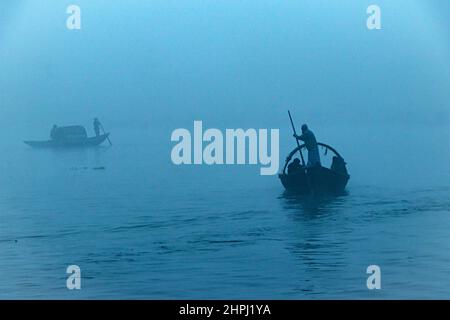 Narayanganj, Dhaka, Bangladesch. 22nd. Februar 2022. Arbeiter überqueren den Fluss Shitalakhya auf Holzbooten, um an einem nebligen Wintermorgen in Narayanganj, Bangladesch, ihren Arbeitsplatz zu erreichen. Dieser Fluss wird täglich von Millionen von Arbeitern als Route in das dicht besiedelte Stadtgebiet genutzt. Die Holzschiffe werden verwendet, um Menschen über den Fluss Shitalakhya zu transportieren, der am Rande der Stadt Narayanganj fließt. (Bild: © Joy Saha/ZUMA Press Wire) Stockfoto