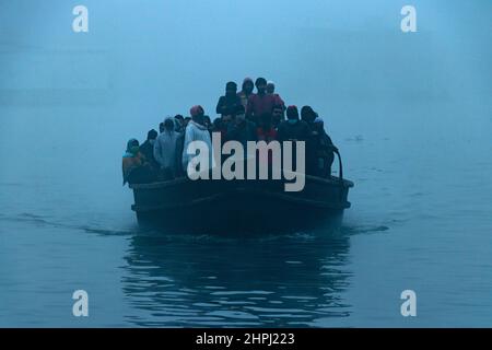 Narayanganj, Dhaka, Bangladesch. 22nd. Februar 2022. Arbeiter überqueren den Fluss Shitalakhya auf Holzbooten, um an einem nebligen Wintermorgen in Narayanganj, Bangladesch, ihren Arbeitsplatz zu erreichen. Dieser Fluss wird täglich von Millionen von Arbeitern als Route in das dicht besiedelte Stadtgebiet genutzt. Die Holzschiffe werden verwendet, um Menschen über den Fluss Shitalakhya zu transportieren, der am Rande der Stadt Narayanganj fließt. (Bild: © Joy Saha/ZUMA Press Wire) Stockfoto