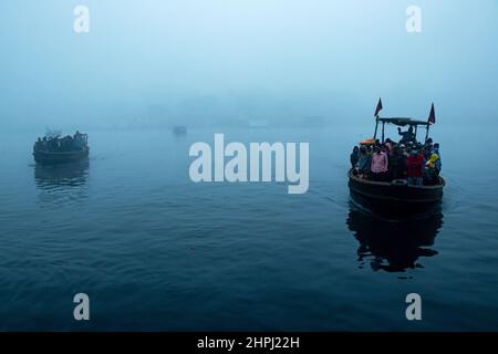 Narayanganj, Dhaka, Bangladesch. 22nd. Februar 2022. Arbeiter überqueren den Fluss Shitalakhya auf Holzbooten, um an einem nebligen Wintermorgen in Narayanganj, Bangladesch, ihren Arbeitsplatz zu erreichen. Dieser Fluss wird täglich von Millionen von Arbeitern als Route in das dicht besiedelte Stadtgebiet genutzt. Die Holzschiffe werden verwendet, um Menschen über den Fluss Shitalakhya zu transportieren, der am Rande der Stadt Narayanganj fließt. (Bild: © Joy Saha/ZUMA Press Wire) Stockfoto