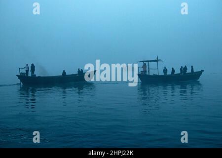 Narayanganj, Dhaka, Bangladesch. 22nd. Februar 2022. Arbeiter überqueren den Fluss Shitalakhya auf Holzbooten, um an einem nebligen Wintermorgen in Narayanganj, Bangladesch, ihren Arbeitsplatz zu erreichen. Dieser Fluss wird täglich von Millionen von Arbeitern als Route in das dicht besiedelte Stadtgebiet genutzt. Die Holzschiffe werden verwendet, um Menschen über den Fluss Shitalakhya zu transportieren, der am Rande der Stadt Narayanganj fließt. (Bild: © Joy Saha/ZUMA Press Wire) Stockfoto