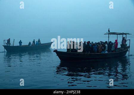 Narayanganj, Dhaka, Bangladesch. 22nd. Februar 2022. Arbeiter überqueren den Fluss Shitalakhya auf Holzbooten, um an einem nebligen Wintermorgen in Narayanganj, Bangladesch, ihren Arbeitsplatz zu erreichen. Dieser Fluss wird täglich von Millionen von Arbeitern als Route in das dicht besiedelte Stadtgebiet genutzt. Die Holzschiffe werden verwendet, um Menschen über den Fluss Shitalakhya zu transportieren, der am Rande der Stadt Narayanganj fließt. (Bild: © Joy Saha/ZUMA Press Wire) Stockfoto