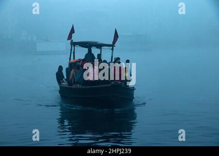 Narayanganj, Dhaka, Bangladesch. 22nd. Februar 2022. Arbeiter überqueren den Fluss Shitalakhya auf Holzbooten, um an einem nebligen Wintermorgen in Narayanganj, Bangladesch, ihren Arbeitsplatz zu erreichen. Dieser Fluss wird täglich von Millionen von Arbeitern als Route in das dicht besiedelte Stadtgebiet genutzt. Die Holzschiffe werden verwendet, um Menschen über den Fluss Shitalakhya zu transportieren, der am Rande der Stadt Narayanganj fließt. (Bild: © Joy Saha/ZUMA Press Wire) Stockfoto