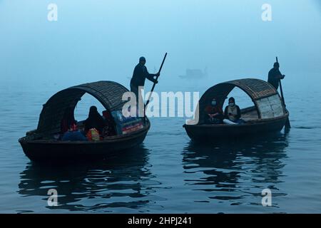 Narayanganj, Dhaka, Bangladesch. 22nd. Februar 2022. Arbeiter überqueren den Fluss Shitalakhya auf Holzbooten, um an einem nebligen Wintermorgen in Narayanganj, Bangladesch, ihren Arbeitsplatz zu erreichen. Dieser Fluss wird täglich von Millionen von Arbeitern als Route in das dicht besiedelte Stadtgebiet genutzt. Die Holzschiffe werden verwendet, um Menschen über den Fluss Shitalakhya zu transportieren, der am Rande der Stadt Narayanganj fließt. (Bild: © Joy Saha/ZUMA Press Wire) Stockfoto