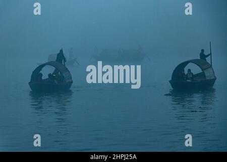 Narayanganj, Dhaka, Bangladesch. 22nd. Februar 2022. Arbeiter überqueren den Fluss Shitalakhya auf Holzbooten, um an einem nebligen Wintermorgen in Narayanganj, Bangladesch, ihren Arbeitsplatz zu erreichen. Dieser Fluss wird täglich von Millionen von Arbeitern als Route in das dicht besiedelte Stadtgebiet genutzt. Die Holzschiffe werden verwendet, um Menschen über den Fluss Shitalakhya zu transportieren, der am Rande der Stadt Narayanganj fließt. (Bild: © Joy Saha/ZUMA Press Wire) Stockfoto