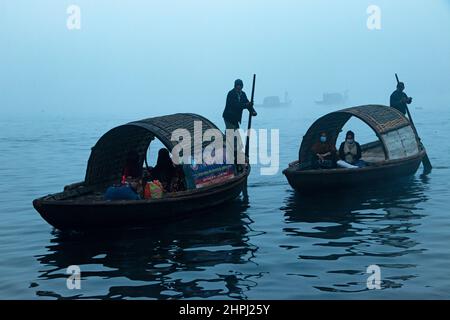 Narayanganj, Dhaka, Bangladesch. 22nd. Februar 2022. Arbeiter überqueren den Fluss Shitalakhya auf Holzbooten, um an einem nebligen Wintermorgen in Narayanganj, Bangladesch, ihren Arbeitsplatz zu erreichen. Dieser Fluss wird täglich von Millionen von Arbeitern als Route in das dicht besiedelte Stadtgebiet genutzt. Die Holzschiffe werden verwendet, um Menschen über den Fluss Shitalakhya zu transportieren, der am Rande der Stadt Narayanganj fließt. (Bild: © Joy Saha/ZUMA Press Wire) Stockfoto