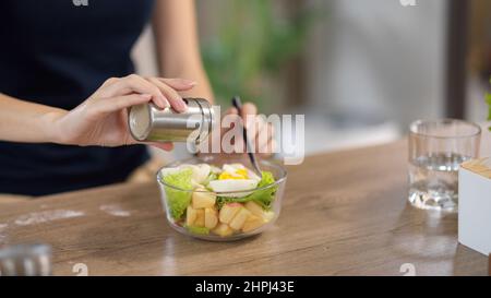 Nahaufnahme, eine Frau, die Salz in ihre gesunde Salatschüssel am heimischen Esstisch gab. Gesunde Ernährung und Konzept der Ernährung Stockfoto