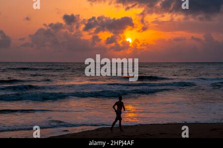 Beobachten Sie den Sonnenuntergang an einem Strand in thailand, und ein Mann joggt am Strand entlang, Thailand. Stockfoto