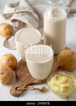 Kartoffelmilch in Gläsern auf weißem Holzhintergrund. Vegane Milch in Glas gießen, mit Kartoffelpüree und Kartoffelknollen auf dem Hintergrund. Speicherplatz kopieren. Hausgemachte Kartoffelmilch aus gekochten Kartoffeln Stockfoto