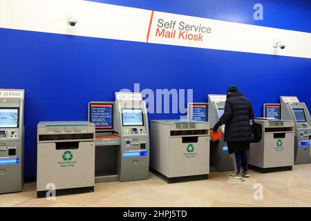 Eine Person verwendet einen Automated Postal Center Self-Service-Kiosk in einem Postamt, um ein Paket zu versenden. Stockfoto