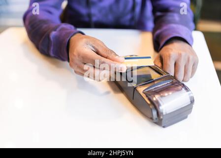 Hoher Winkel der Ernte anonymen afroamerikanischen männlichen Café-Client für die Bestellung mit Kunststoff-Kreditkarte über Terminal bezahlen Stockfoto