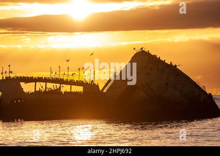 Ein wunderschöner Sonnenuntergang über dem Strand in der Nähe von Aptos, Kalifornien, der den alten, verödnisten Pier und ein altes Schiffswrack hervorhebt. Stockfoto