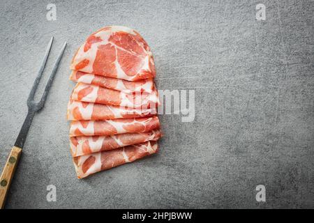 Italienischer getrockneter Schinken. Coppa Stagionata mit Gabel auf einem Küchentisch. Draufsicht. Stockfoto