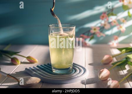 Kollagenpulver wird mit einem Löffel in ein Glas Wasser gegeben Stockfoto