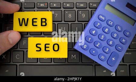 Draufsicht auf Web- und SEO-Text auf Holzblöcken mit Laptop und Rechner-Hintergrund. Stockfoto
