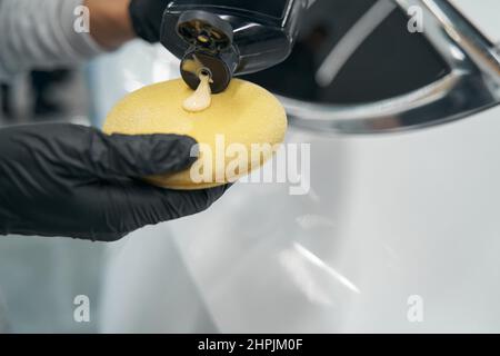 Hände mit Handschuhen, die flüssiges Wachs auf Schaumschwamm auftragen Stockfoto