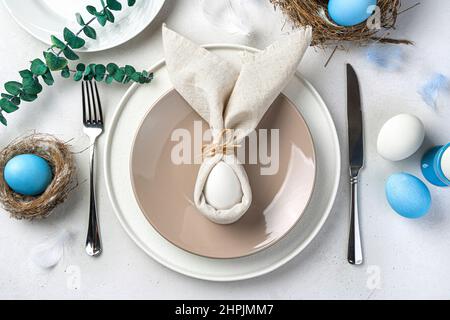 Frohe Ostern. Festliches Servieren des Ostertisches mit einem Osterhasen aus Servietten und Eiern. Draufsicht. Stockfoto