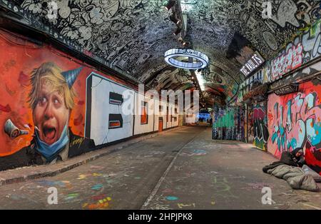 Graffiti, auf denen der britische Premierminister Boris Johnson eine Partei hat, steht im Gegensatz zu einem Obdachlosen, der auf dem gegenüberliegenden Bürgersteig rau schläft Stockfoto