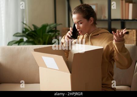 Junge Frau, die ein Gespräch mit dem Lieferservice über das Mobiltelefon geführt hat, öffnete die Schachtel mit der falschen Reihenfolge Stockfoto