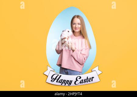 Eierrahmen in der Mitte der Grußkarte mit glücklichen jungen schönen weiblichen in rosa Pullover und blaue Jeans halten Osterhase Stockfoto