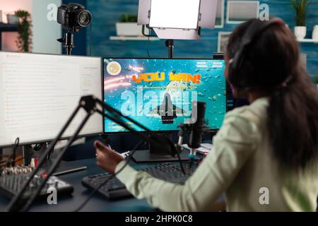 Gamer Frau gewinnt Weltraum-Shooter-Videospiele Wettbewerb im Gespräch mit Spielern mit Mikrofon während Live-Streaming, erfolgreiche Gewinnerin Online-Videospiele mit RGB-Computer spielen Stockfoto
