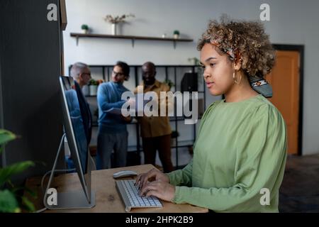 Junge hübsche biracial Geschäftsfrau Blick auf Computer-Bildschirm während der Vorbereitung für die Präsentation oder Analyse von Finanzdaten Stockfoto