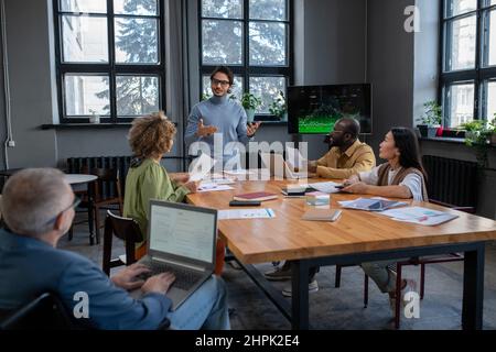 Junger, selbstbewusster Business Coach, der vor Publikum die Datenanalyse präsentiert und mit Kollegen darüber diskutiert Stockfoto