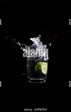 Wasser spritzt aus dem Glas durch abgeworfene Zitrone auf schwarzem Hintergrund. Selektiver Fokus verwendet. Stockfoto