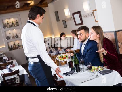 Verärgerte Gäste, die im Restaurant mit dem Kellner in Konflikt stehen Stockfoto