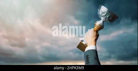Erfolgreicher Geschäftsmann mit Trophäe in der Hand auf Himmel Hintergrund. Geschäftserfolg und Leistungskonzept. Copy space Stockfoto
