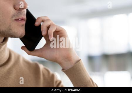 Teil des Gesichts und der Hand eines jungen Geschäftsführers oder Managers mit Smartphone per Ohr, der mit einem Untergebenen oder Kunden kommuniziert Stockfoto
