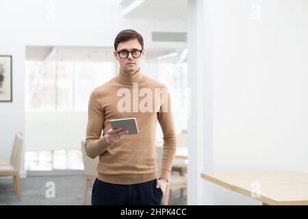 Junge, selbstbewusste Unternehmerin mit smarter Casualwear, die ein digitales Tablet hält, während sie im Internet arbeitet und Online-Daten analysiert Stockfoto