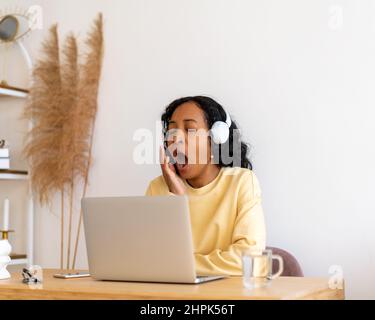 afroamerikanische Studentin gähnend, während sie sich Online-Vorträge über Kopfhörer auf dem Laptop anhört Stockfoto