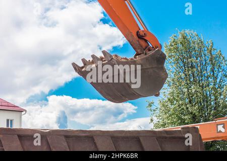 Aushubarbeiten. Der Eimer des Traktors lädt den Boden mit einer Schaufel in die Rückseite eines Muldenkipper auf der Baustelle. Stockfoto
